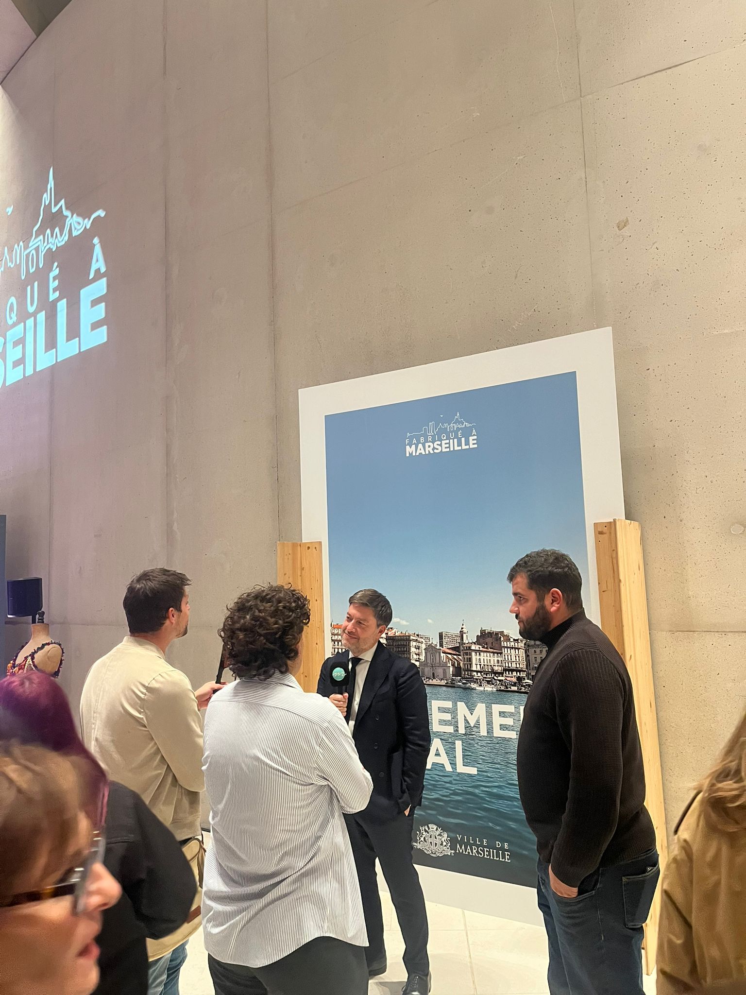 Interview lors de la cérémonie du label Fabriqué à Marseille, devant l’affiche officielle de la Ville de Marseille.